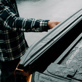 Das Roll in Cover bei Regen, wobei Wassertropfen darauf perlen und eine Person demonstriert das sich die Heckklappe des Ford Ranger EXC auch bei geschlossenem Rollo öffnen lässt.